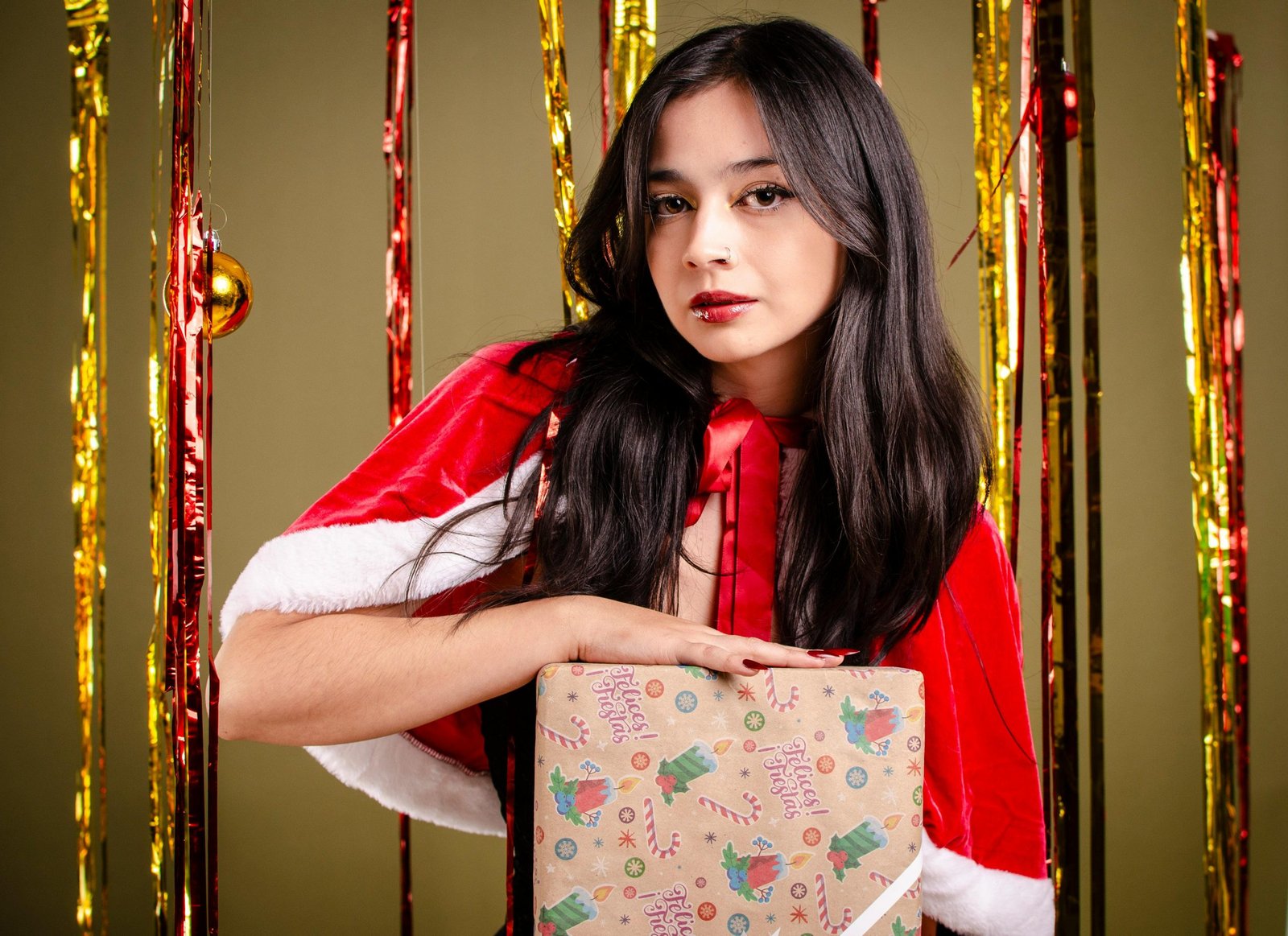 A stylish portrait of a woman in a Santa outfit holding a Christmas gift, set against a festive backdrop.